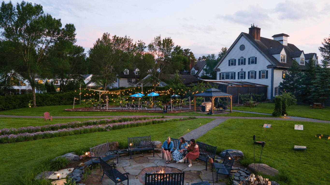 Seen from above, an inn with a fire pit in the evening with people sitting around.