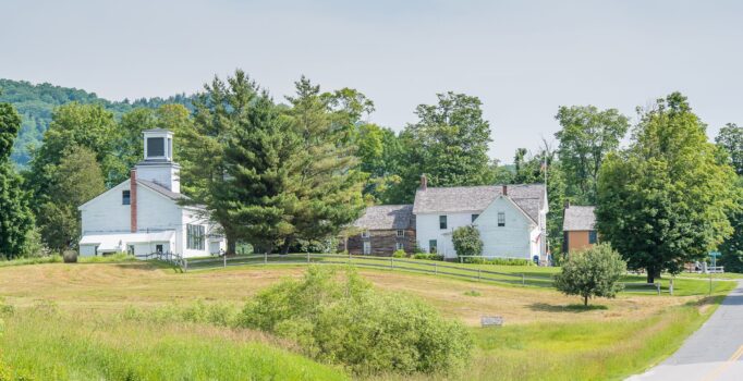 Scenic rural landscape with a white church, trees, rolling hills, and a road.