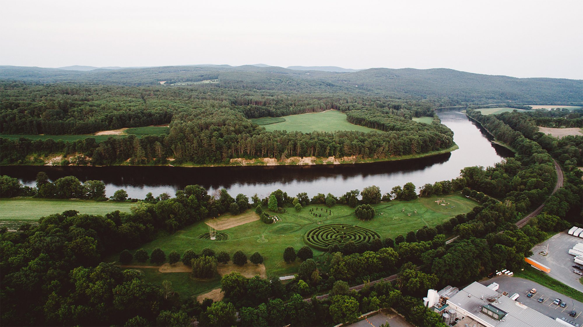 Seen from above, a labyrinth built into green grass next to a river with mountains and trees visible.