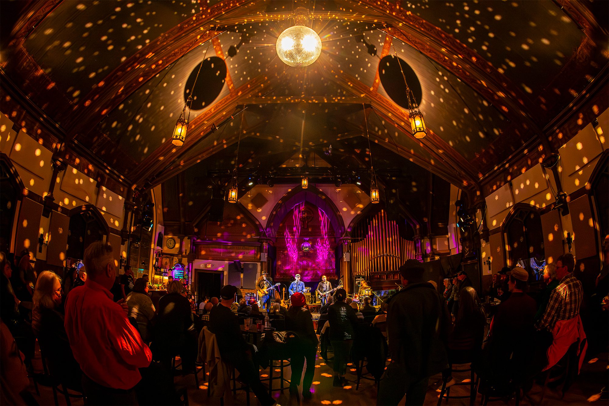 People perform on stage with bright lights all around and an energetic crowd. 