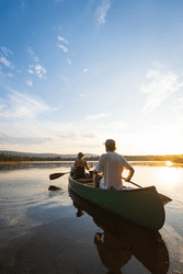 Two people seen from behind paddling a canoe on water on a sunny summer day.
