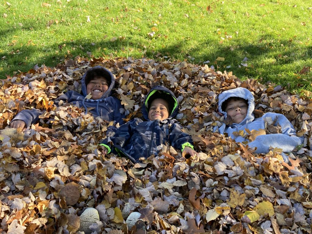 Three children smiling in a pile of leaves outside in the fall.