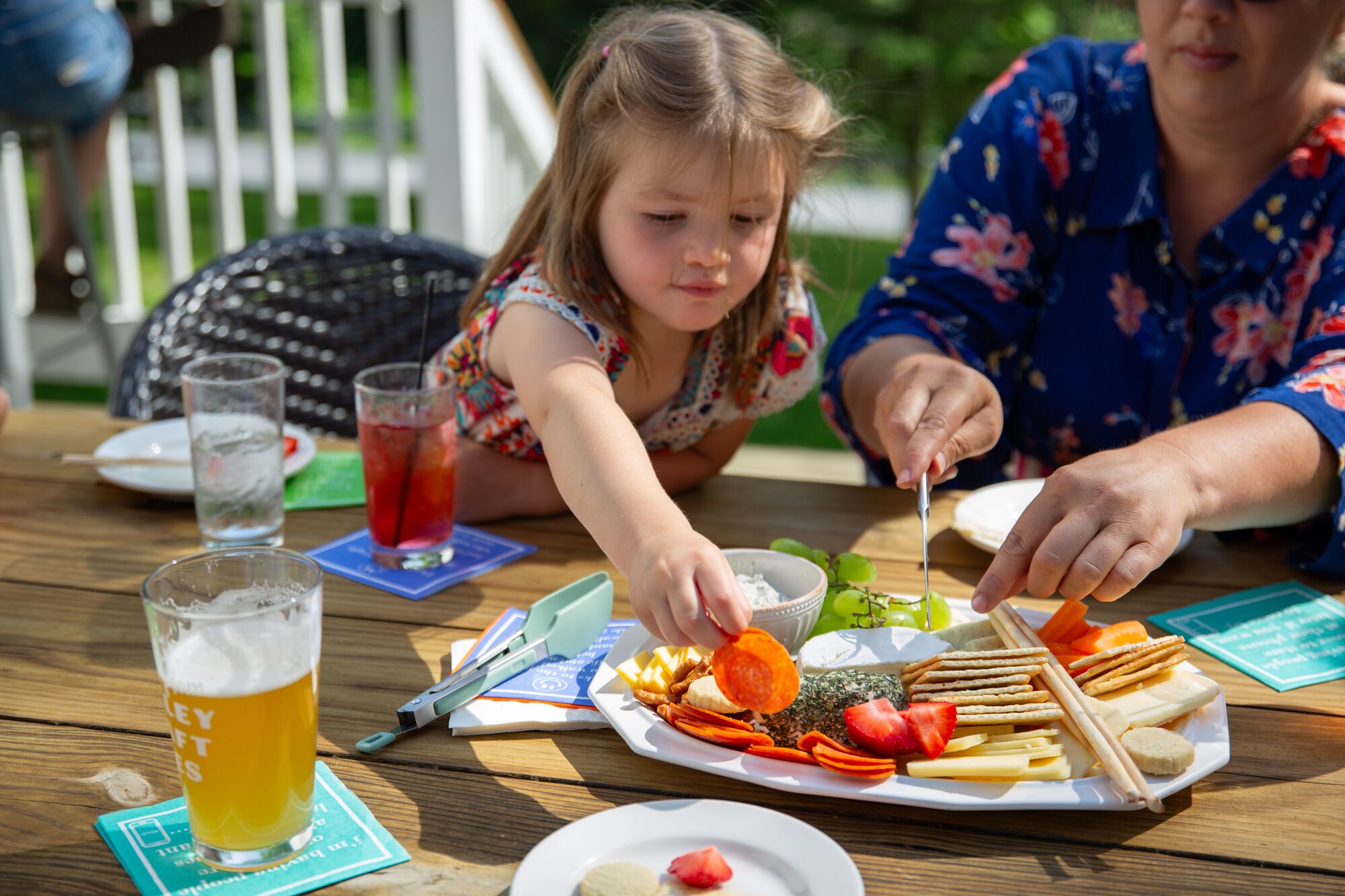 Child reaching across table to pick up a carrot off of a white plate of cheese, crackers and vegetables