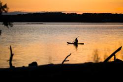 A person paddling a kayak on a lake in the sunset.