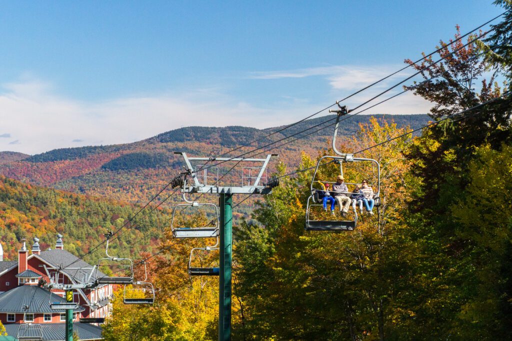 People on a chairlift looking at fall foliage from above on a sunny day. 