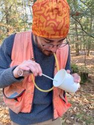A person smiles whilst performing field work in a forest outside in the summer.