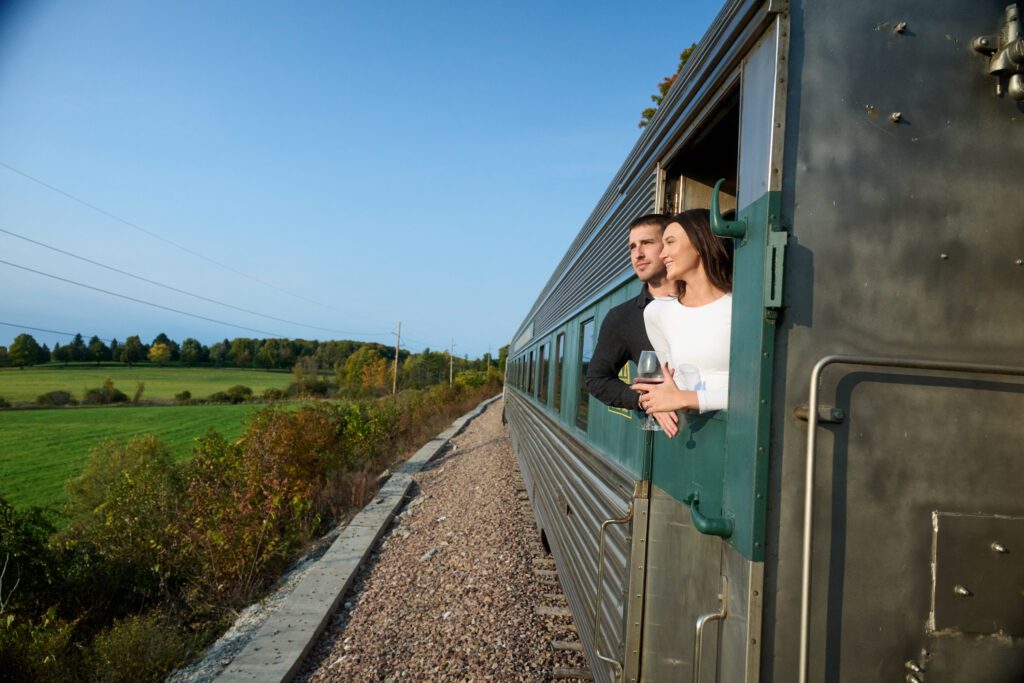 Two people lean out of the window of a train car in Vermont.