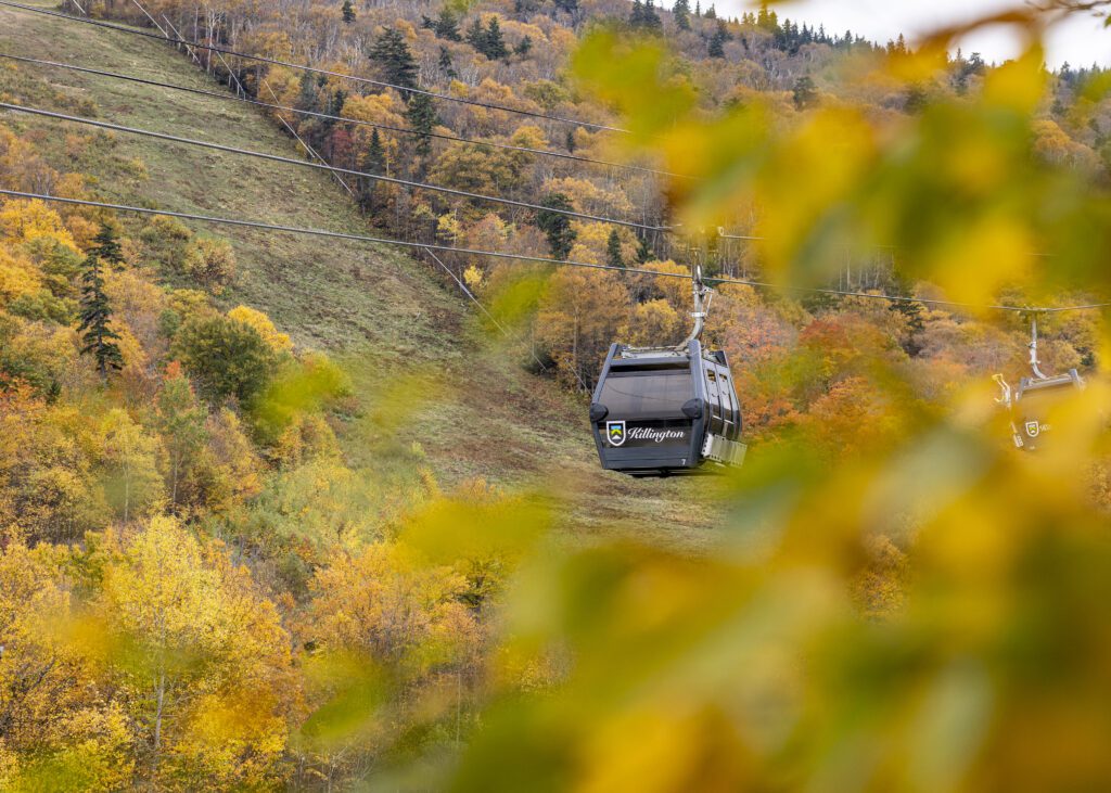 A gondola chair lift surrounded by red, yellow and orange fall foliage.