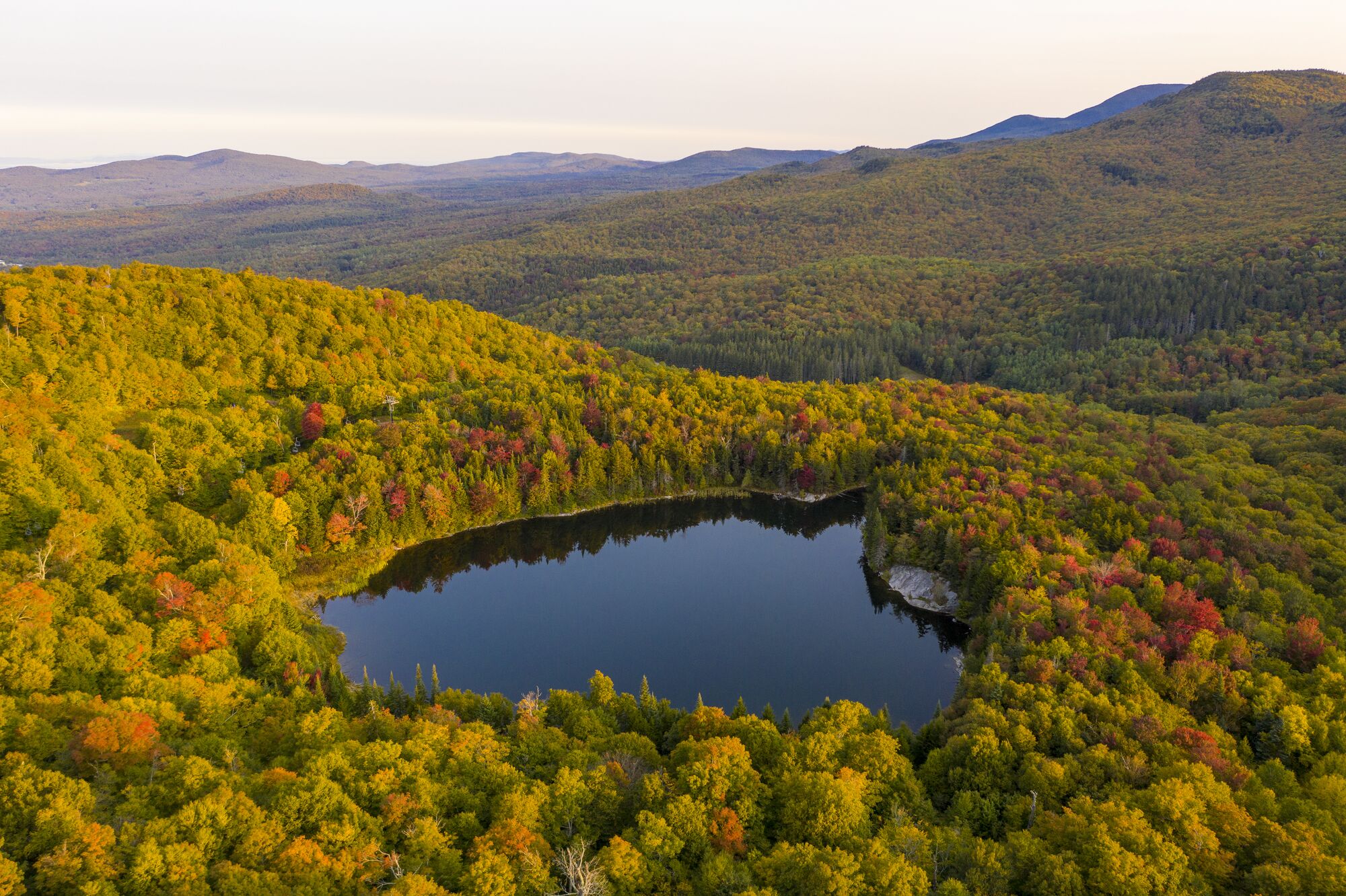 Viewed from above, a small lake among hills with colorful foliage in Vermont.
