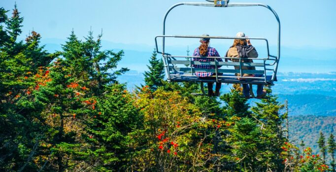 Two people enjoy a scenic chairlift ride above fall foliage in Vermont.
