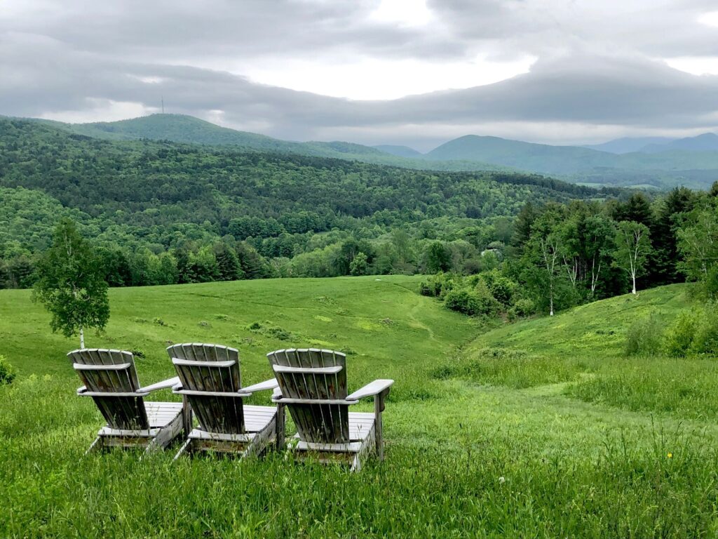 Three Adirondak chairs facing green mountains.