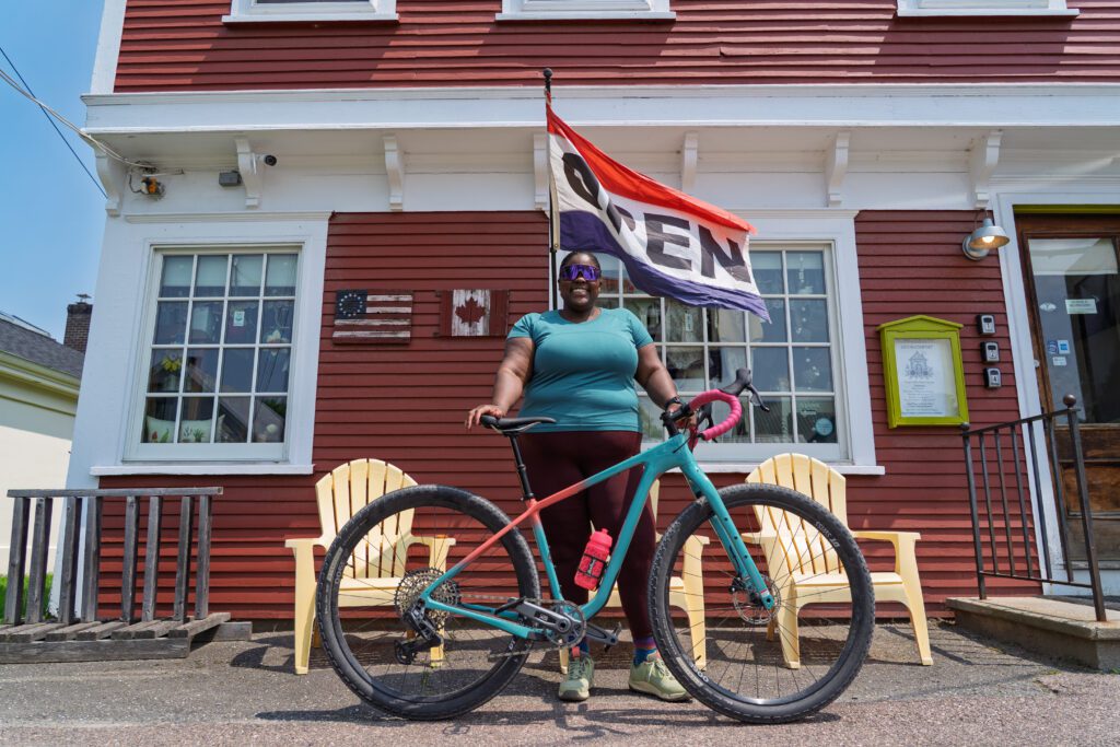 A woman stands with a bicycle in front of a country store in Vermont.