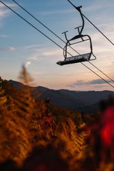 A chair lift surrounded by red, yellow and orange fall foliage.