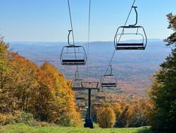 A chair lift surrounded by red, yellow and orange fall foliage.