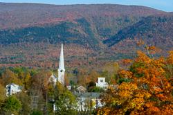 View of a white steeple and hills with colorful foliage in the distance.