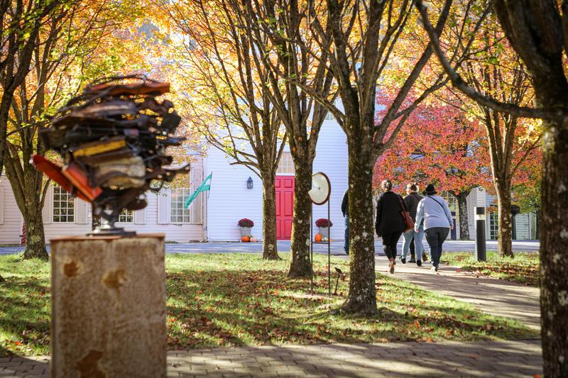 People walk on a tress lined path past a sculpture in Vermont.