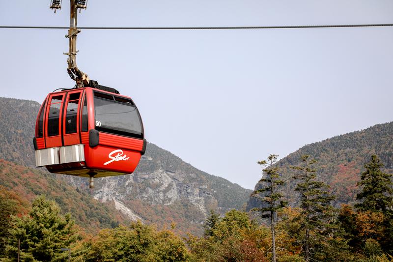 A red gondola chair lift passes through colorful fall foliage in Vermont.