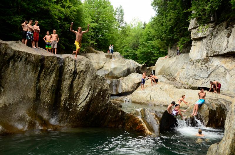 Children jumping off a rock into a river and swimming.