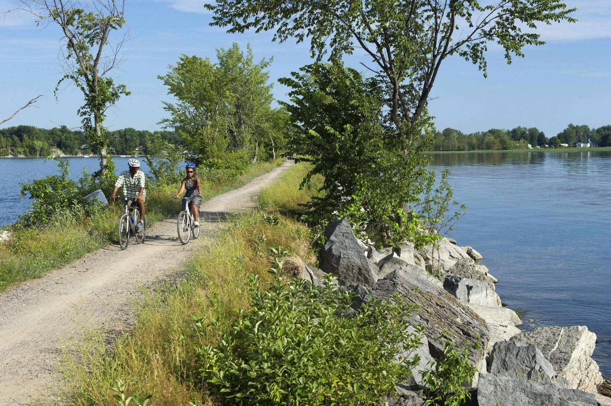 Two people ride bicycles on a causeway by a lake in Vermont.