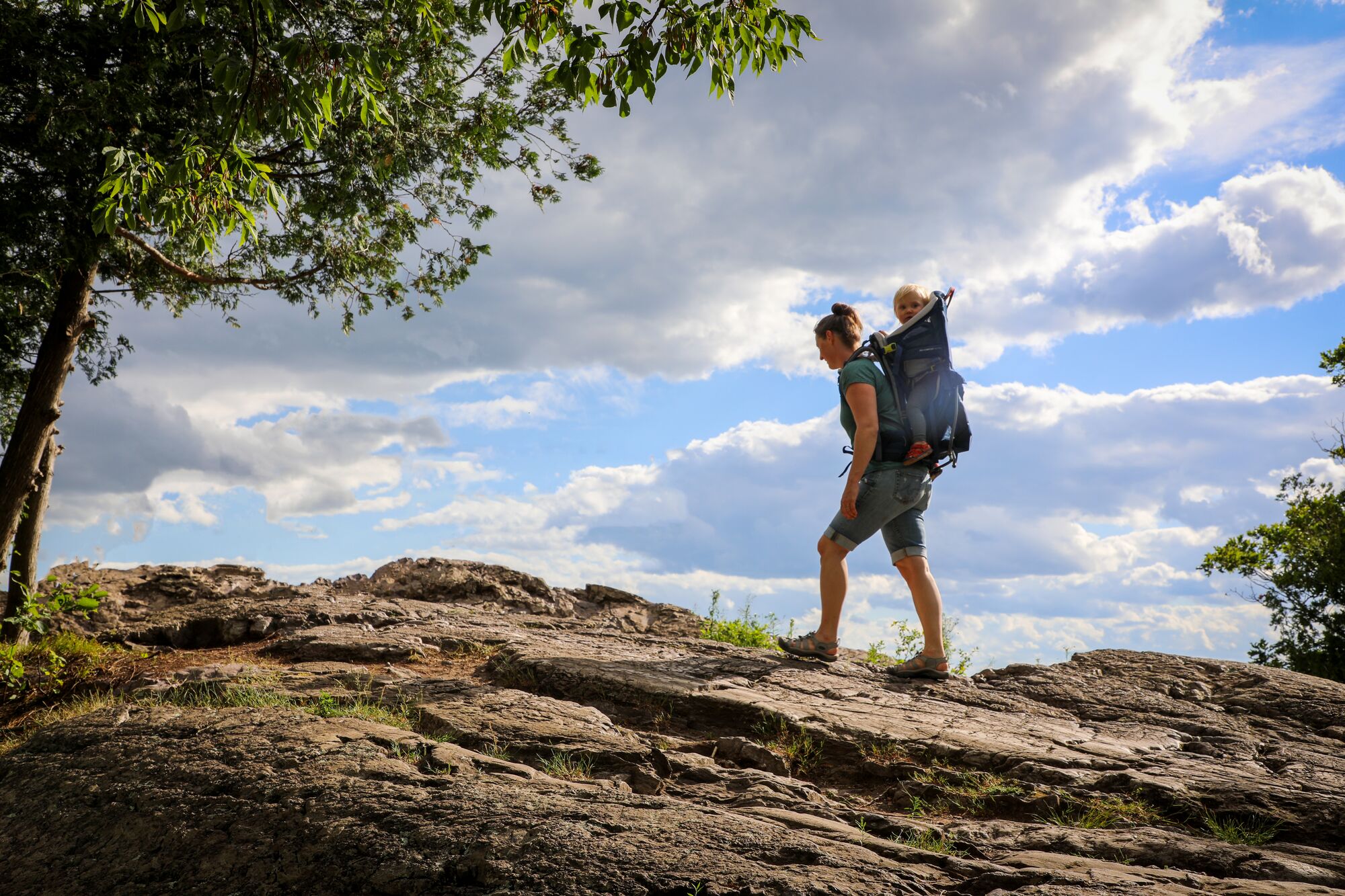 A person with a child in a back carrier climbs a mountain ridge in Vermont.