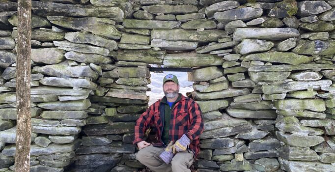 A person sits in a stone structure outside in the winter.