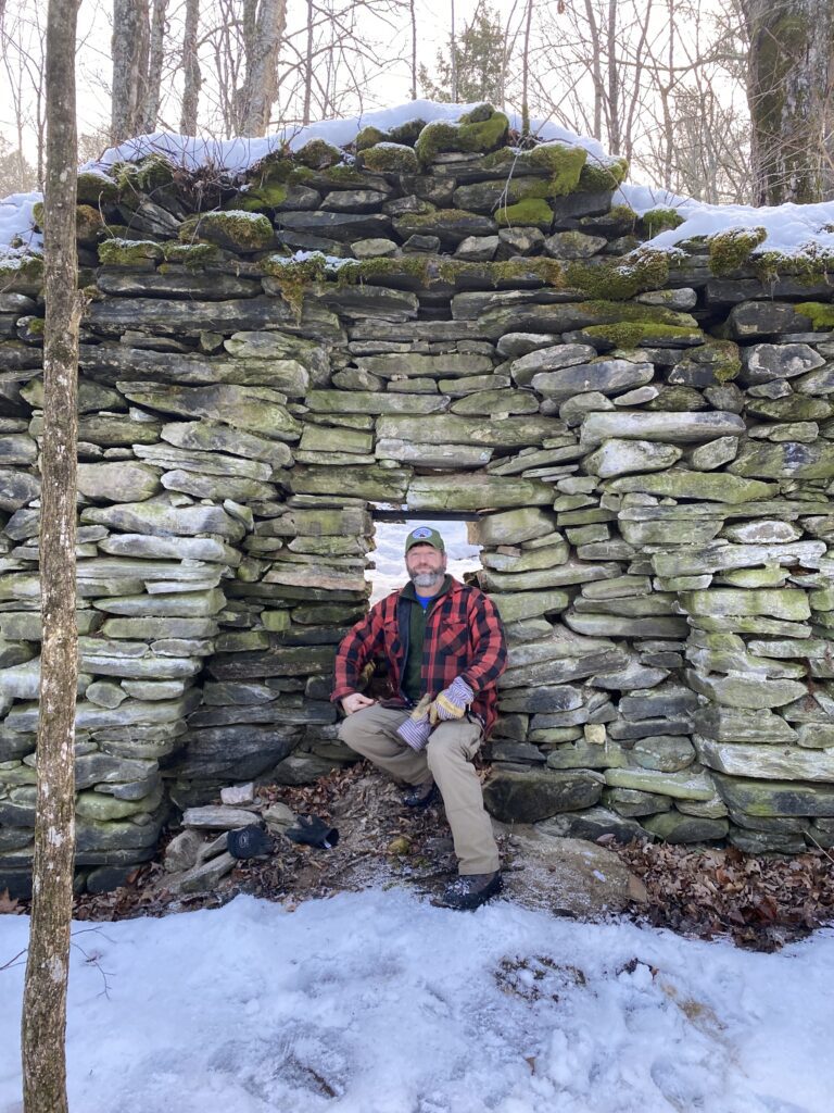 A person sits in a stone structure outside in the winter.