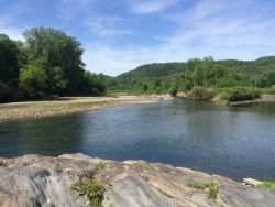 A serene river curves through lush green landscapes, flanked by hills under a clear blue sky, with rocky terrain in the foreground.