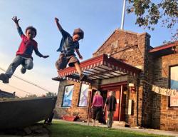 Two children jump off a rock in front of a building in Vermont.
