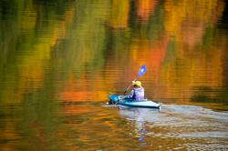 A kayaker paddles on a pond among fall foliage in Vermont.