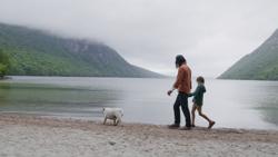 A person and a child walk a dog along a lake in Vermont.