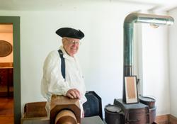 A person in a historic costume stands next to a stove in Vermont.