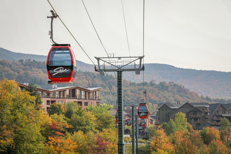 A red gondola ski lift passes through colorful fall foliage in Vermont.