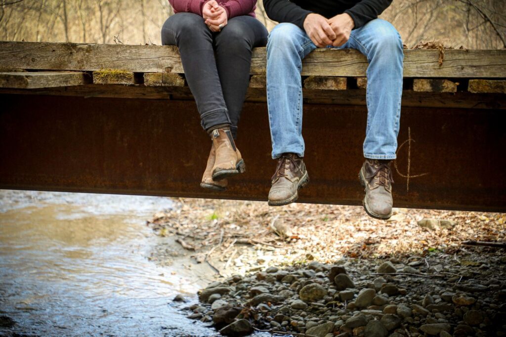 two people dangle their feet off a trail bridge in Vermont.