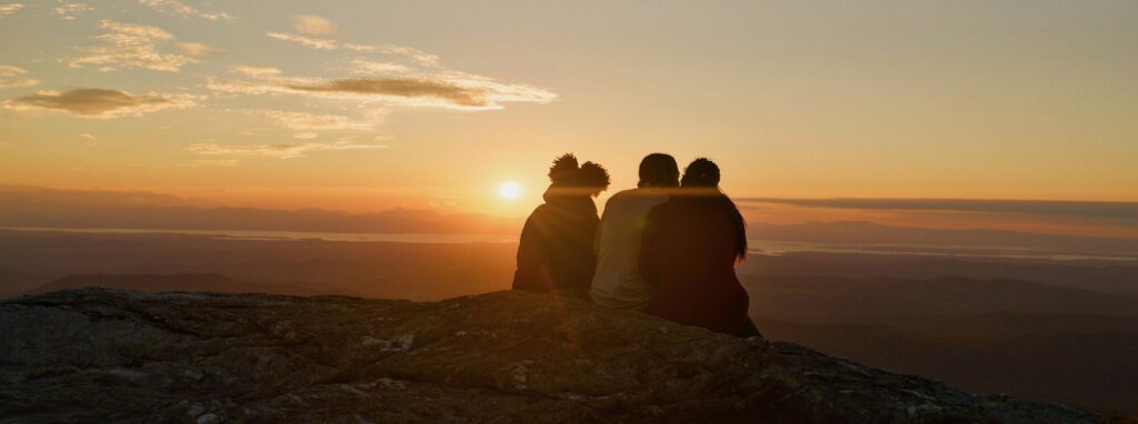 Three people enjoy a sunset from a mountaintop in Vermont.