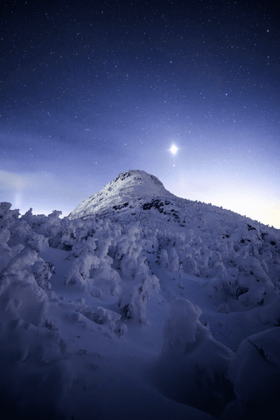 A planet rises brightly above a snow-covered mountain at night.