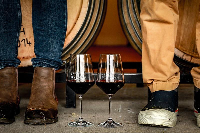 A close-up photo of two people's boots next to glasses of wine.