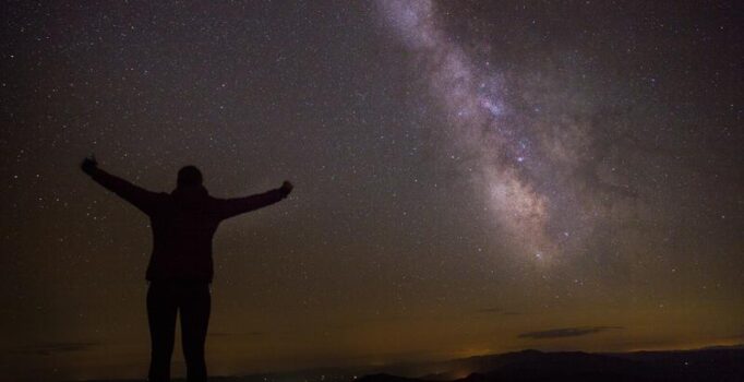A person stands with arms wide looking at the stars in Vermont.