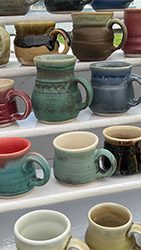 Colorful handmade pottery is lined up on shelves at an outdoor market. 