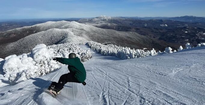  A person snowboards down a freshly groomed trail on a sunny day with a blue sky.