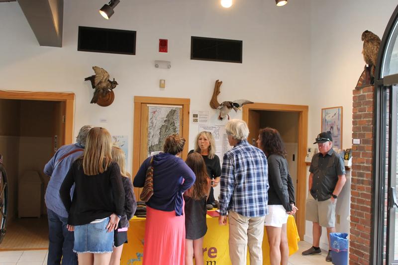 A group of visitors gathers around an information desk to speak with a staff member inside a visitor center with maps and wildlife mounts on the wall.