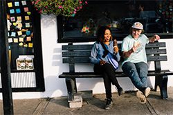 Two people sit outside on a bench eating soft ice cream in cones.