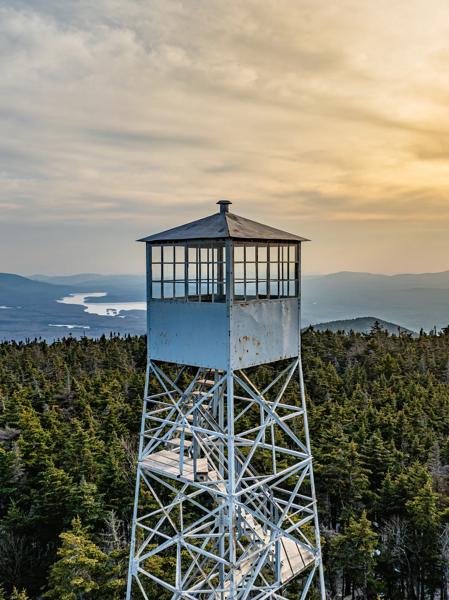 A fire tower seen from exterior at sunset on top of a mountain on a summer evening.