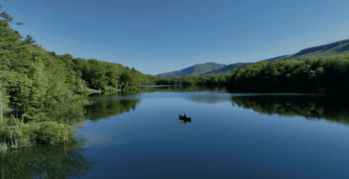 A high-angle scenic view of the lush, rolling Green Mountains of Vermont under a bright summer sky with scattered white clouds.