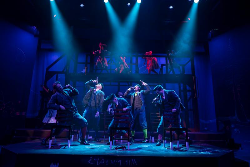 Performers dance on stage under bright blue spotlights during a dramatic theatrical production.