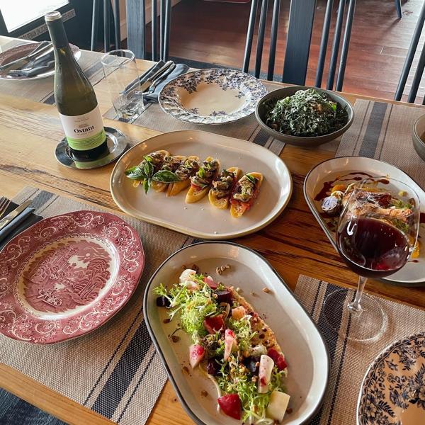 Various colorful dishes of food are on a wooden table along with a bottle indoors.