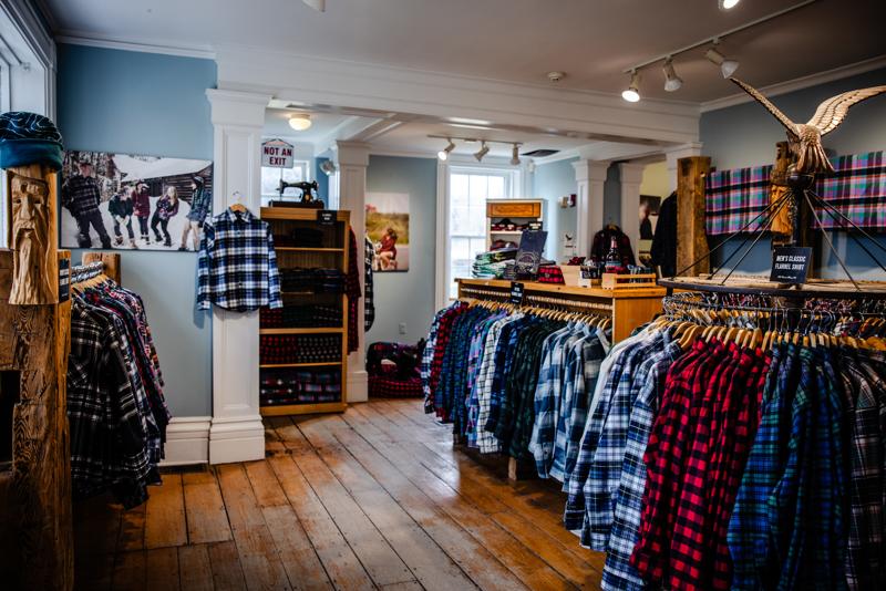 The interior of a Vermont Flannel Co. store featuring clothing racks filled with colorful plaid and flannel shirts on wooden floors.