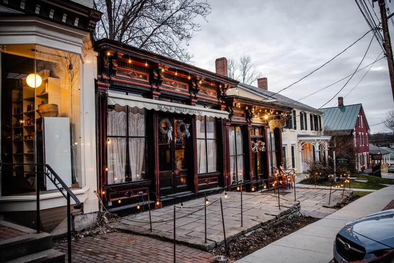 The exterior storefront of the Black Sheep Bistro in Vergennes, Vermont, adorned with warm string lights along a brick sidewalk.