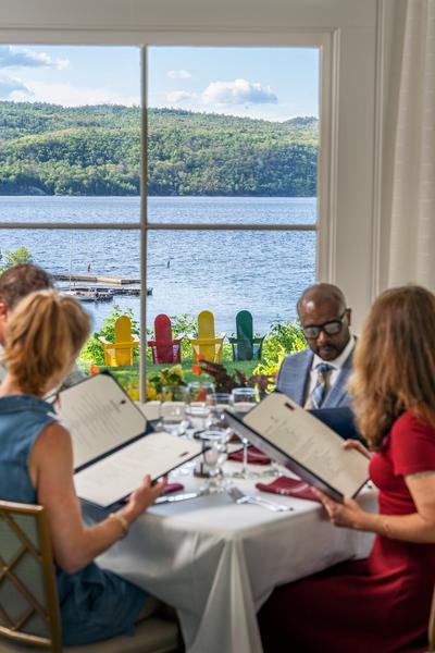 Patrons viewing menus at a white tablecloth dining table next to a large window overlooking Lake Champlain at Ardelia's restaurant.