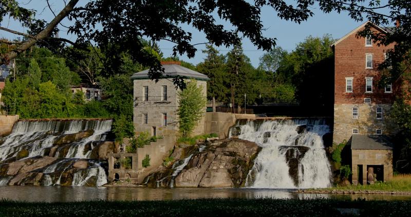 Scenic view of the cascading waterfall at Vergennes Falls Park on Otter Creek, flanked by historic stone and brick mill buildings.