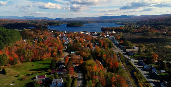 A downtown seen from above with red foliage brightening trees. A lake and mountains are in the distance.